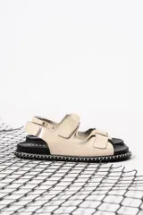 Sandalias planas color nude con tiras anchas con ajuste de velcro y suela negra con detalle de costuras blancas.