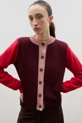 Saco de punto con diseño color block, presenta cuerpo en color bordó, mangas en color rojo y tapeta frontal con cuello redondo en color rosado. Posee cierre frontal con botones y puños acanalados.