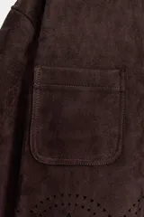 Chaqueta de cuello solapa y manga larga, color marrón oscuro, con efecto ante. Presenta bolsillos delanteros de plastrón, cierre frontal con botones y un bajo troquelado con diseño floral y acabado festoneado.