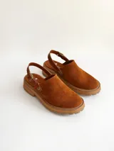 Zueco de cuero gamuzado color óxido, con tira trasera ajustable mediante hebilla metálica. Presenta una suela de plataforma con textura acanalada y detalle de textura reptil en la tira posterior.