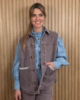 Chaleco de denim color marrón, confeccionado en 100% algodón, con bolsillos frontales amplios, cierre de botones y costuras decorativas bordadas en blanco en los bordes y los bolsillos.