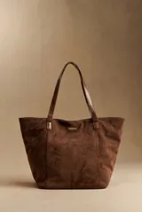 Bolso tipo shopper de gamuza sintética marrón con asas largas de ecuero brillante y detalle de placa metálica dorada con logo en el frente.