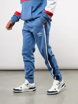 Pantalon de jogging azul de felpa, con franjas laterales en blanco y azul marino. Presenta el escudo del Club Nacional de Football en el muslo derecho y el logo de Umbro en el izquierdo.