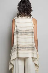 Cardigan sin mangas confeccionado en algodón con tejido texturizado y bajo asimétrico. Presenta bordes deshilachados, bordados detallados y adornos de monedas doradas a lo largo de las solapas.