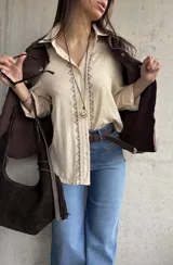 Camisa beige de tejido liviano y calce relajado, con manga larga y detalle de puntilla y bordado en contraste que recorre el frente.