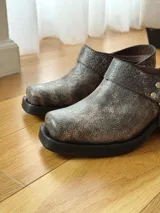 Zueco de cuero con efecto desgastado en tono visón, con diseño de punta cuadrada, suela gruesa negra y detalle de correa con tachas metálicas y argolla lateral.