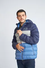 Campera puffer con diseño color block en tonos azul marino, gris y azul claro. Cuenta con capucha, cierre frontal completo, bolsillos laterales con cierre y logo estampado en el pecho.