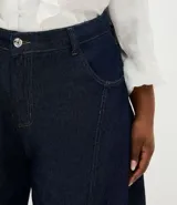Pantalón de jean raw azul oscuro, corte barrel con piernas anchas y cintura cónica. Presenta costuras contrastantes, cierre tradicional con botón y bolsillos laterales.