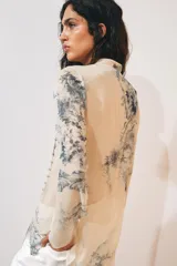 Camisa de cuello redondo y manga larga con diseño de estampado artístico en tonos azules sobre fondo beige. Presenta un cierre frontal asimétrico con botones forrados a tono y una abertura lateral en el escote.