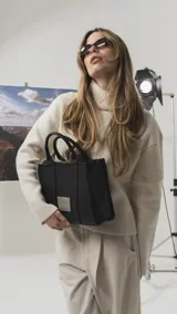 Cartera estructurada de tamaño mediano, confeccionada en símil cuero color negro. Presenta doble asa de mano, correa larga ajustable y desmontable, y un bolsillo trasero con cierre. El compartimento principal cuenta con cierre, división interna y bolsillos organizadores.