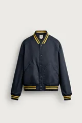 Cazadora bomber estilo universitario, de corte relaxed fit y tejido técnico azul marino, con cuello, puños y dobladillo de rib elástico a rayas amarillas. Cuenta con bolsillos delanteros de plastrón y cierre frontal con botones a presión.