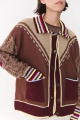 Cardigan de punto con diseño multicolor en tonos marrones, bordó y detalles en amarillo y celeste. Presenta cuello tipo polo, cierre frontal con botones, bolsillos aplicados en el frente y mangas con trama trenzada y coderas bordadas.