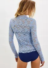 Blusa de encaje transparente color celeste, con escote en V y mangas largas. Presenta un diseño ajustado con textura floral y costuras que realzan la silueta.