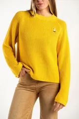 Sweater de punto en color amarillo, con diseño oversize, cuello redondo y manga larga. Presenta un pequeño bordado de un velero en la parte superior del pecho.