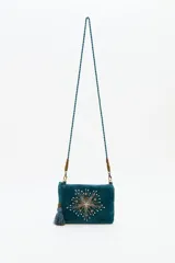 Cartera tipo bandolera de terciopelo color verde petróleo, con bordado central de estrellas en pedrería y mostacillas. Incluye una borla decorativa lateral y correa trenzada con detalles metálicos.