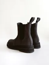 Bota tipo Chelsea de caña media, confeccionada en cuero negro con acabado mate. Presenta paneles elásticos laterales, tiradores traseros y suela track robusta con plataforma dentada.