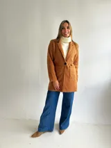 Abrigo estilo sastrero de textura tipo bouclé en color camel, con cierre frontal de un botón, solapas clásicas y bolsillos frontales tipo plaqué.