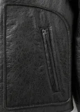 Chaqueta efecto piel de color negro con diseño oversize, cuello camisero y forro interior de borreguito marrón. Cuenta con cierre frontal de cremallera, manga larga y dos bolsillos de parche laterales.