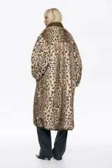 Abrigo largo reversible de corte línea A, con una cara de pelo sintético con estampado animal print y otra cara de tela técnica lisa en tono beige. Presenta capucha, cierre frontal con cremallera y botones de presión, y bolsillos laterales con cremallera.