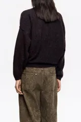 Jersey de punto en mezcla de mohair y lana, color negro con efecto jaspeado. Presenta un escote en V decorado con una aplicación de encaje negro y mangas largas con corte holgado.