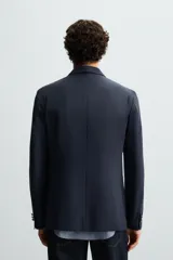 Blazer regular fit color azul marino, confeccionada en tejido con lana. Presenta cuello con solapas de pico, manga larga con puño abotonado, bolsillos de vivo en el pecho y de plastrón en la cadera. Incluye un bolsillo interior y aberturas en la espalda. El cierre es frontal con botonadura cruzada.