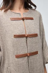 Capa de lana fina sin teñir, con diseño de corte amplio y mangas tipo kimono. Presenta cierre frontal mediante tres alamares de cuero en tono marrón.