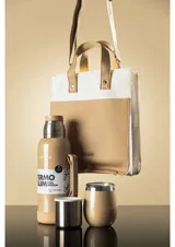 Matera de diseño vertical con combinación de materiales en color beige y marrón. Presenta cuerpo inferior en cuero sintético marrón con logo grabado y sección superior en tejido de lona cruda. Incluye asas cortas de mano en cuero sintético marrón con remaches metálicos.