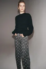 Jeans de tiro medio con corte relajado y largo al tobillo. Presenta un diseño de cinco bolsillos, cierre frontal con cremallera y botón metálico, y un estampado integral de lunares blancos sobre fondo gris oscuro.
