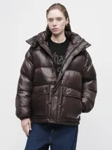 Campera puffer de corte holgado en color marrón oscuro con acabado brillante. Presenta cuello alto, cierre frontal con cremallera y botones a presión, además de bolsillos frontales con solapa.