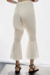Pantalón de tiro alto con cintura elástica, confeccionado en viscosa. Presenta bolsillos de plastrón en el frente, aplicaciones de puntilla y bordados florales a tono, con bajo acabado en volantes.