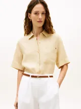 Camisa de manga corta Tommy Hilfiger de corte amplio y color beige, confeccionada en puro lino. Presenta cuello inglés, cierre frontal de botones, un bolsillo de parche en el pecho con el logo bordado y hombros ligeramente caídos.