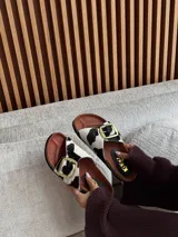 Sandalias bajas con base marrón y dos tiras de pelo con estampado animal print y hebillas doradas.