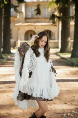 Poncho de lana merino color crudo con cuello alto, diseño amplio y flecos en el ruedo. Presenta bordados decorativos en tono chocolate y detalles de flecos en los hombros.