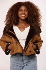 Campera corta tipo gamulán en color negro, con interior y detalles en puños y cuello de corderito sintético al tono. Presenta cierre frontal metálico y un botón decorativo en el ruedo.