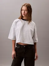 Remera Calvin Klein de corte boxy y largo cropped, con diseño de rayas horizontales, cuello redondo en contraste y mangas cortas con hombros caídos. Presenta un pequeño logo bordado en el pecho.