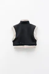 Chaleco biker negro de cuero sintético con forro de borrego beige, cierre frontal metálico, bolsillos laterales con cremallera y cinturón ajustable.