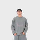 Buzo de manga larga color gris claro, con cuello redondo y diseño holgado. Presenta pequeños estampados gráficos en color rosado en el pecho y en la manga.