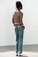 Jeans rectos de tiro medio en denim azul con efecto deslavado. Presentan bandas laterales con detalles brillantes, bolsillos delanteros y traseros, y aberturas en los tobillos con botonadura metálica.