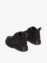 Bota de montaña Dr. Martens modelo Woodard, color negro, con cordones de tipo excursionista en amarillo y negro, cuello acolchado, suela acanalada Club Wedge con pespunte negro y tirador de talón de goma.