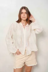 Camisa blanca de manga larga con bordados florales y detalles de ojales, cuello camisero y cierre frontal con botones ocultos.