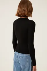 Suéter de punto negro con cuello anudado y abertura sobre el pecho. Presenta detalle de botones a presión con forma de sol en la parte delantera y bordado "TRS".