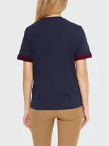 Remera Moncler de algodón azul marino con cuello redondo y manga corta. Presenta puños tejidos con patrón en zigzag rojo y azul marino, y un parche rectangular rojo con el logo de la marca en el borde inferior.