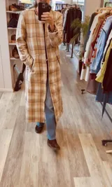 Tapado largo de paño liviano con diseño de cuadros en tonos marrones. Presenta solapas clásicas, bolsillos laterales con detalles en cuero y tajos profundos en los costados.