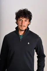 Buzo de cuello alto con cierre frontal parcial, manga larga y puños acanalados. Presenta un diseño liso en color negro con el logo de la marca bordado en el pecho.