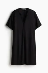 Vestido túnica negro a la rodilla en tejido liviano de viscosa, con cuello mao y abertura en V. Diseño de corte holgado con hombros levemente caídos, mangas cortas y bajo recto con tajos laterales. La parte posterior es ligeramente más larga.