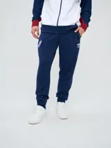 Pantalón deportivo azul marino con puños elásticos en los tobillos, bolsillos laterales con cierre, escudo del Club Nacional de Football en una pierna y logo de Umbro en la otra.