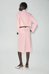 Blazer corto rosado con cuello solapa, hombreras y mangas largas. Cuenta con cierre cruzado delantero con dos botones oscuros y un bolsillo de ojal en el pecho.