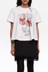 Remera blanca de algodón, de corte línea A con vuelo, escote redondo y mangas cortas. Presenta un estampado frontal con diseño de zapatillas de ballet en tonos grises y lazos rojos.