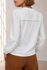 Remera blanca de manga larga con detalles de encaje en el frente y puños elásticos.