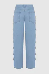 Pantalón de denim estilo wide leg en color azul claro, con tiro alto y detalle de botones dorados decorativos a lo largo de las costuras laterales de las piernas.